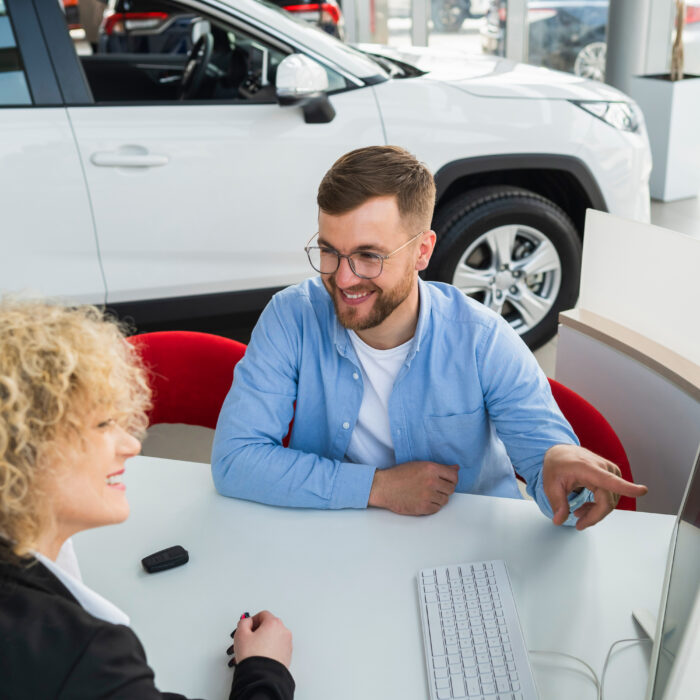 Car dealership manager with client at computer in showroom