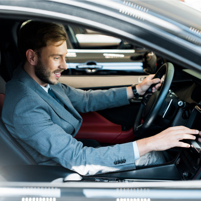 selective focus of cheerful bearded driver sitting on car and touching display